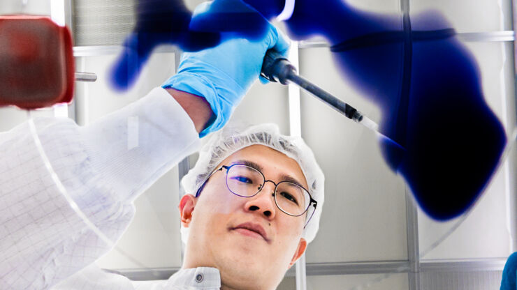 Person i labbrock och handskar häller en blå vätska på en glasyta.