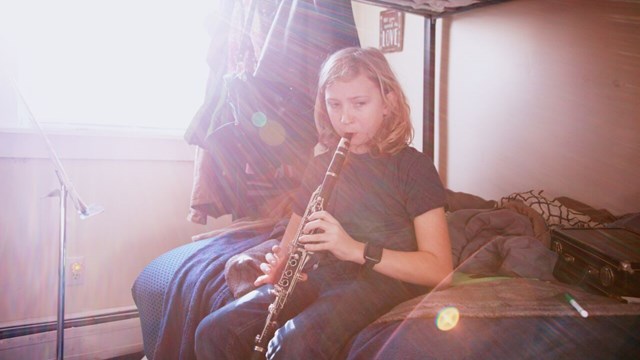 Ett barn sitter i en säng i motljus och övar på att spela klarinett