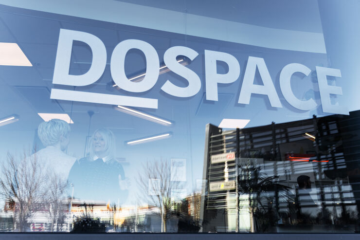 Två kvinnor i samtal bakom en stor glasvägg med ordet Dospace.