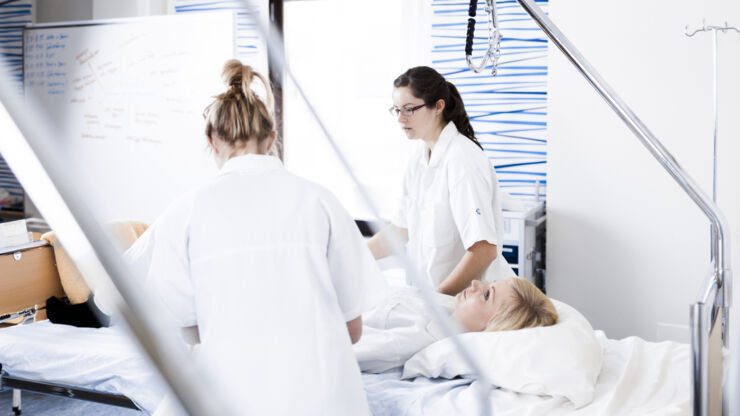 Nursing students care for a patient lying in a hospital bed.