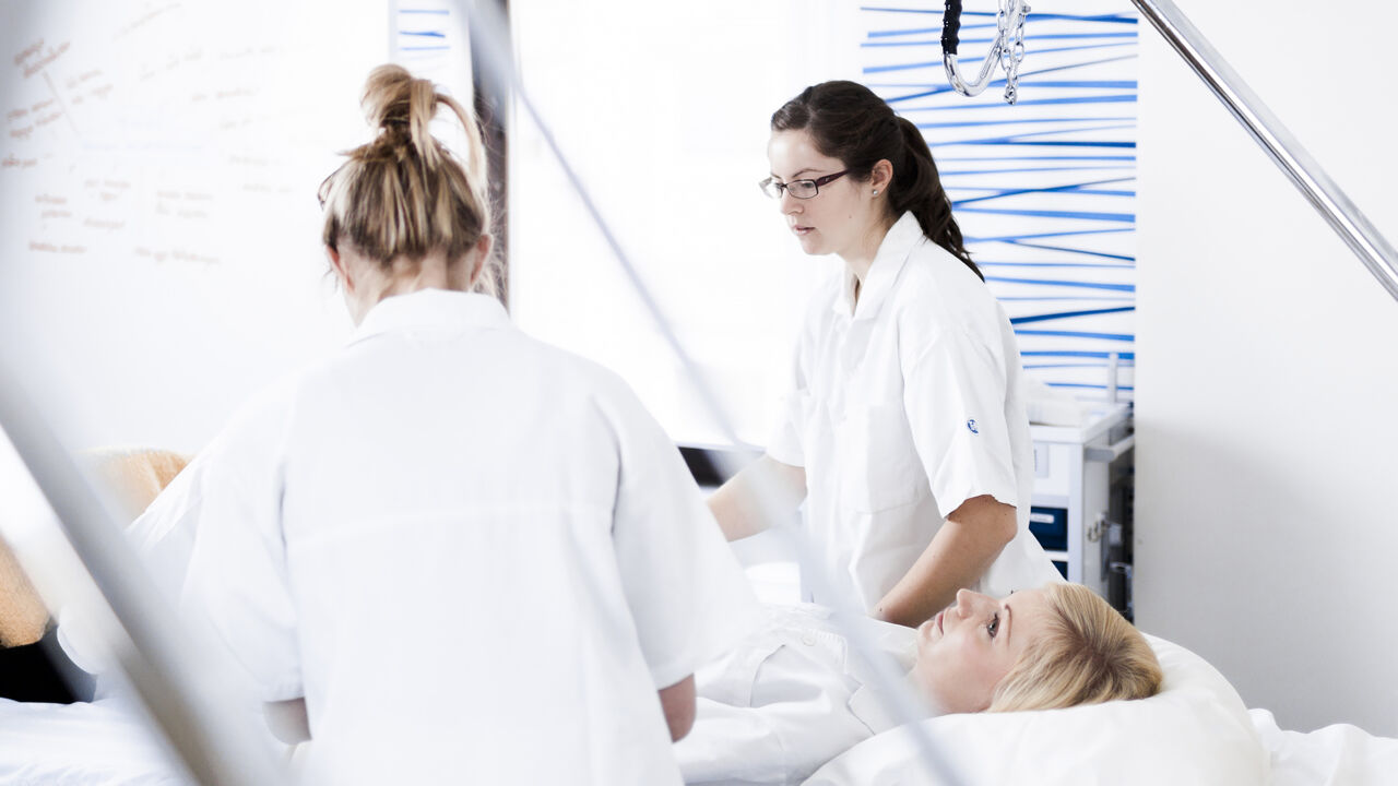 Sjuksköterskestudenter tar hand om en patient som ligger i en sjukhussäng.