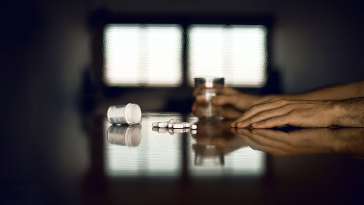 En person har sin hand på bordet där det ligger piller.