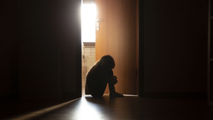 Ett barn sitter ledsen i en mörk lägenhet.