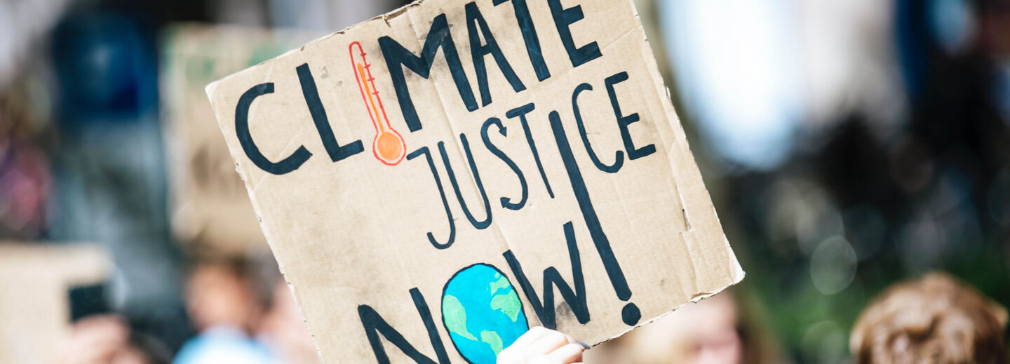 Demonstration. A sign with text in English Climate justice now in the foreground.