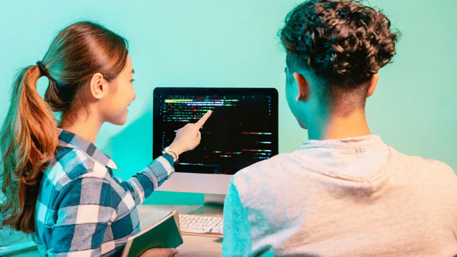 Students discussing programming code at a computer screen