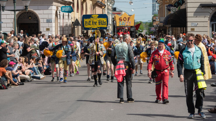 Orkester i gula jackor går längs gata omgiven av folk