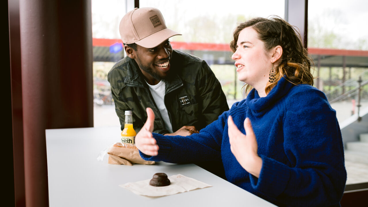 Manlig och kvinnlig student som samtalar och fikar