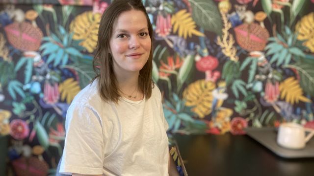 Inomhus porträtt av Ellen Mårtensson som sitter vid ett cafébord. 