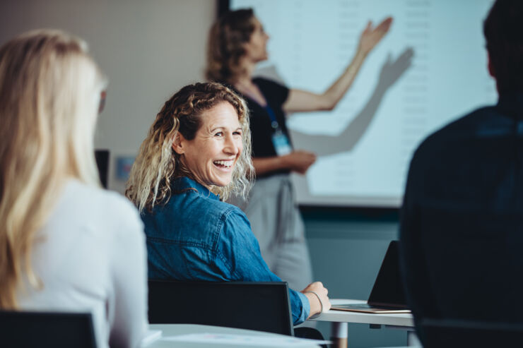 En kvinna skrattar i en klassrumsmiljö.