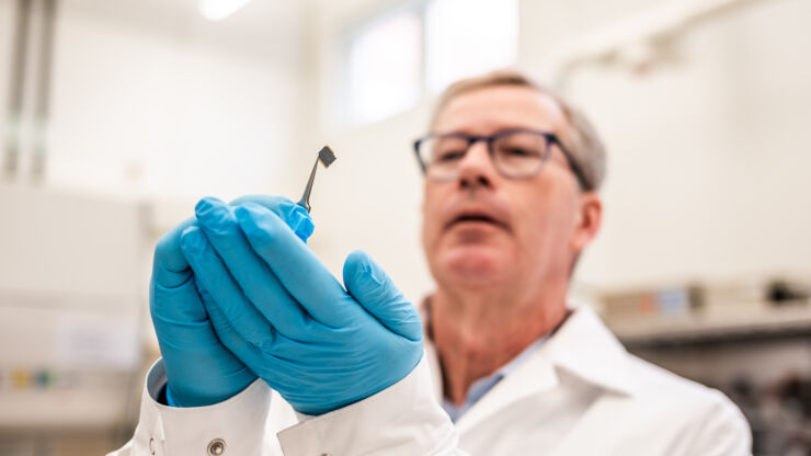 Researcher holds small disc with tweezers close to face.