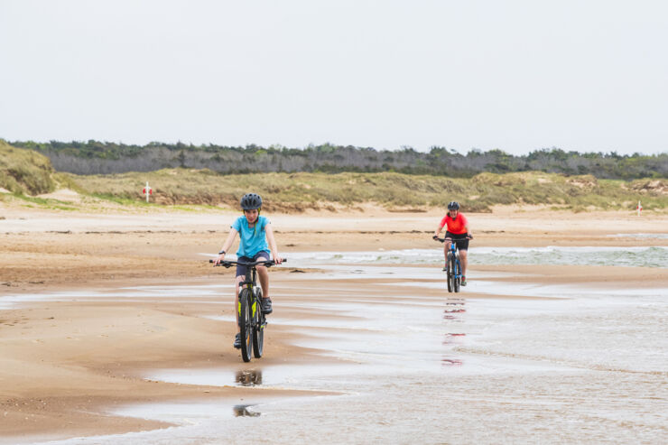 Två barn cyklar efter varandra på en strand