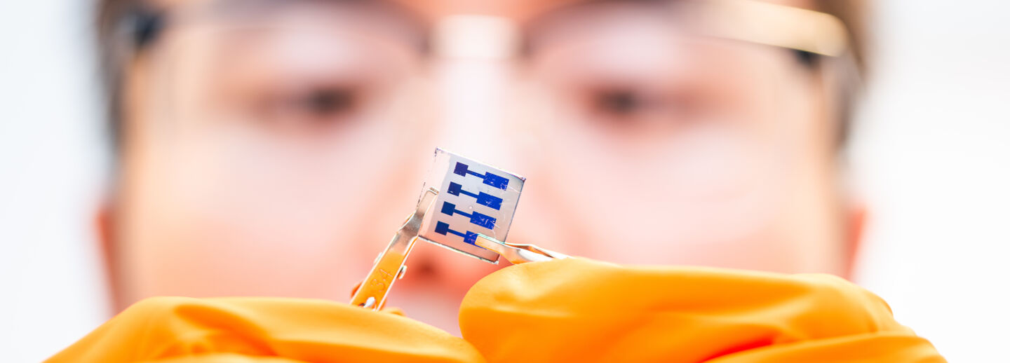 Closeup of electronic component held with tweezers, part of a mans face in the backgound