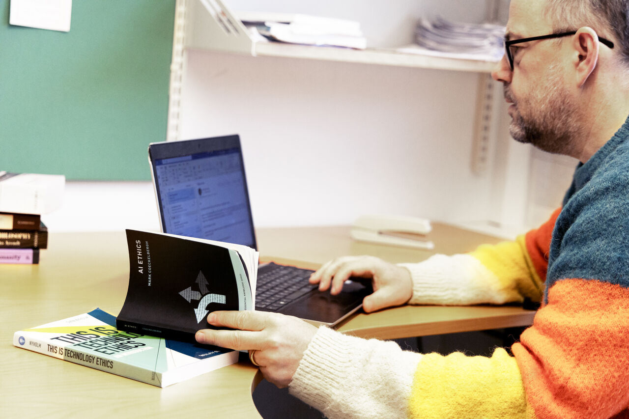 Man sitter framför dator med böcker om AI.