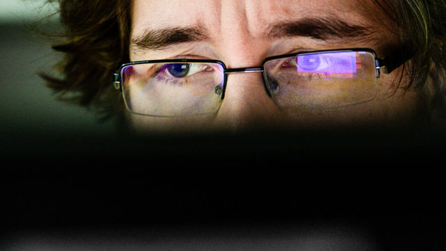 Person with glasses looks at a computerscreen.