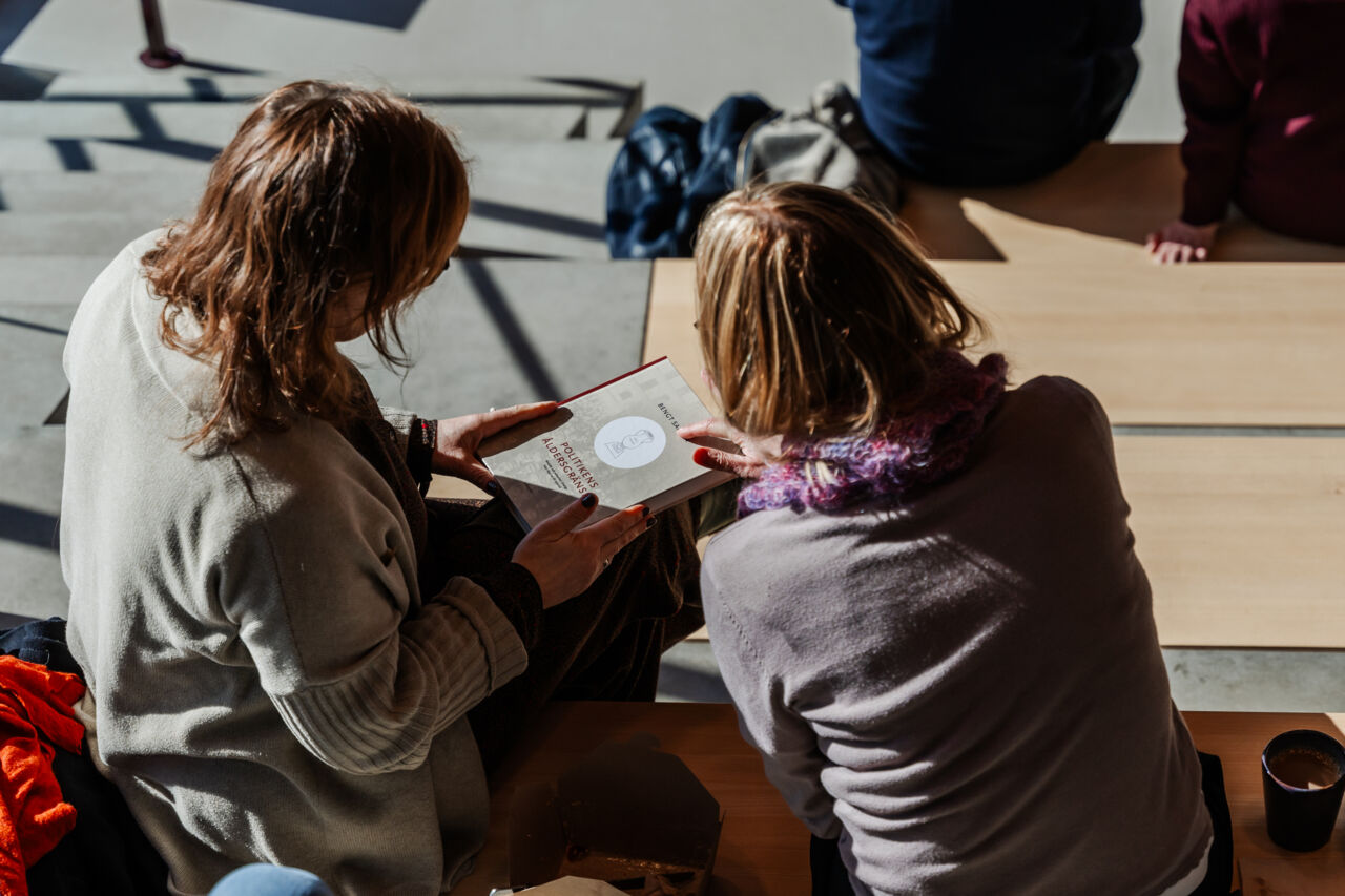 Två åhörare tittar på en bok under en föreläsning