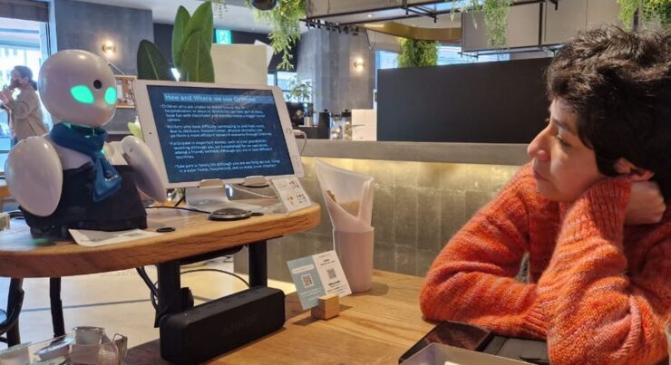 A person is sitting in front of a robot and reading a screen.