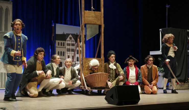 Skådespelare i 1700-talskostymer på en scen med en giljotin