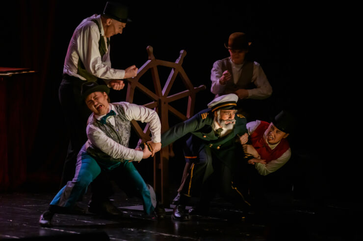En sjökapten omgiven av andra skådespelare på en scen.