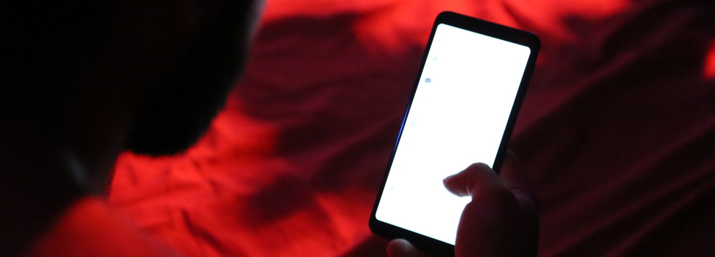 En person håller i en mobiltelefon med ljus skärm  i ett mörkt rum med rött ljus