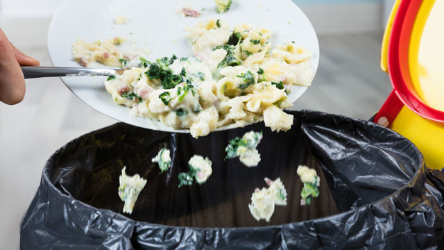 A  person throws leftover pasta in the rubbish bin.