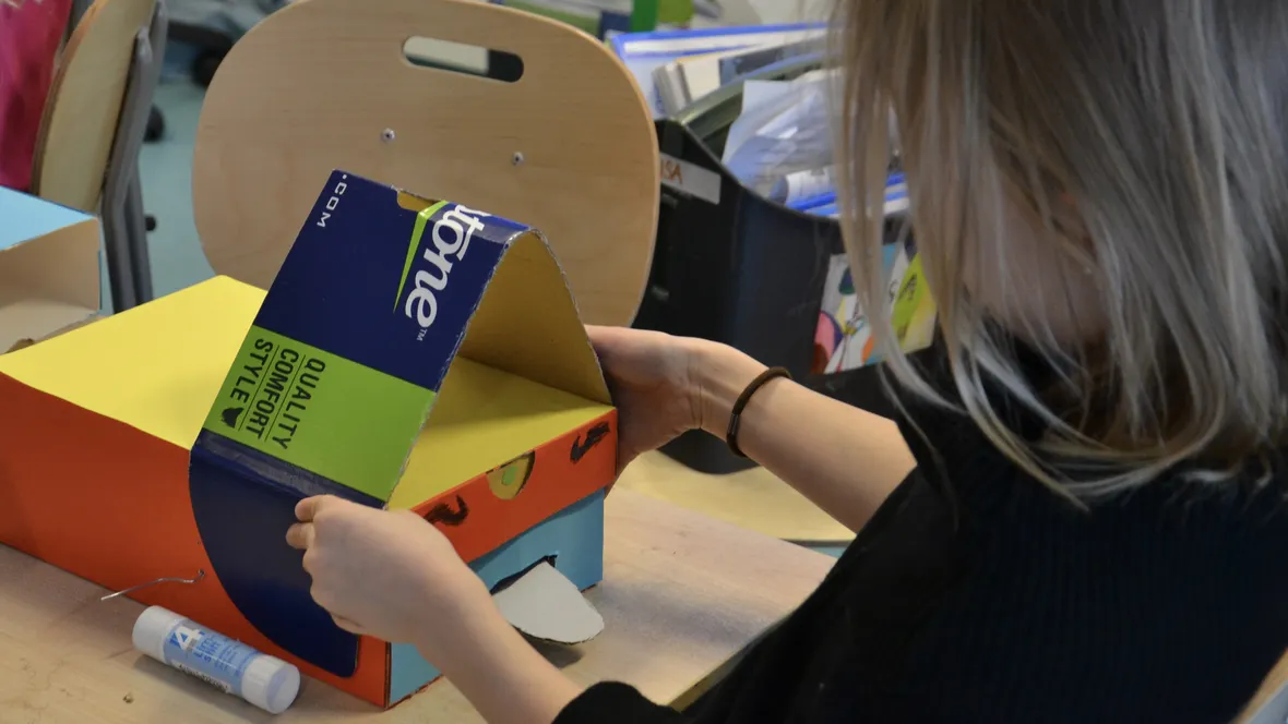 Flicka monterar en pappskiva på en kartong.