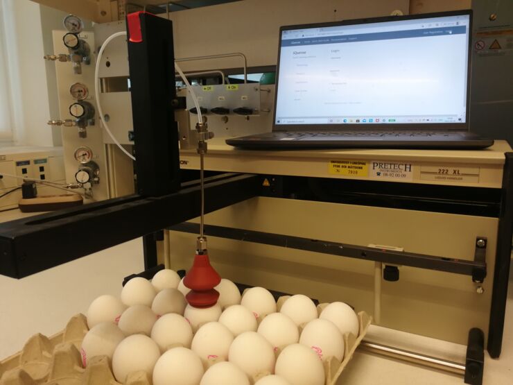 A carton of white eggs in front of a computer screen. A sensor is attached to one of the eggs in the carton.