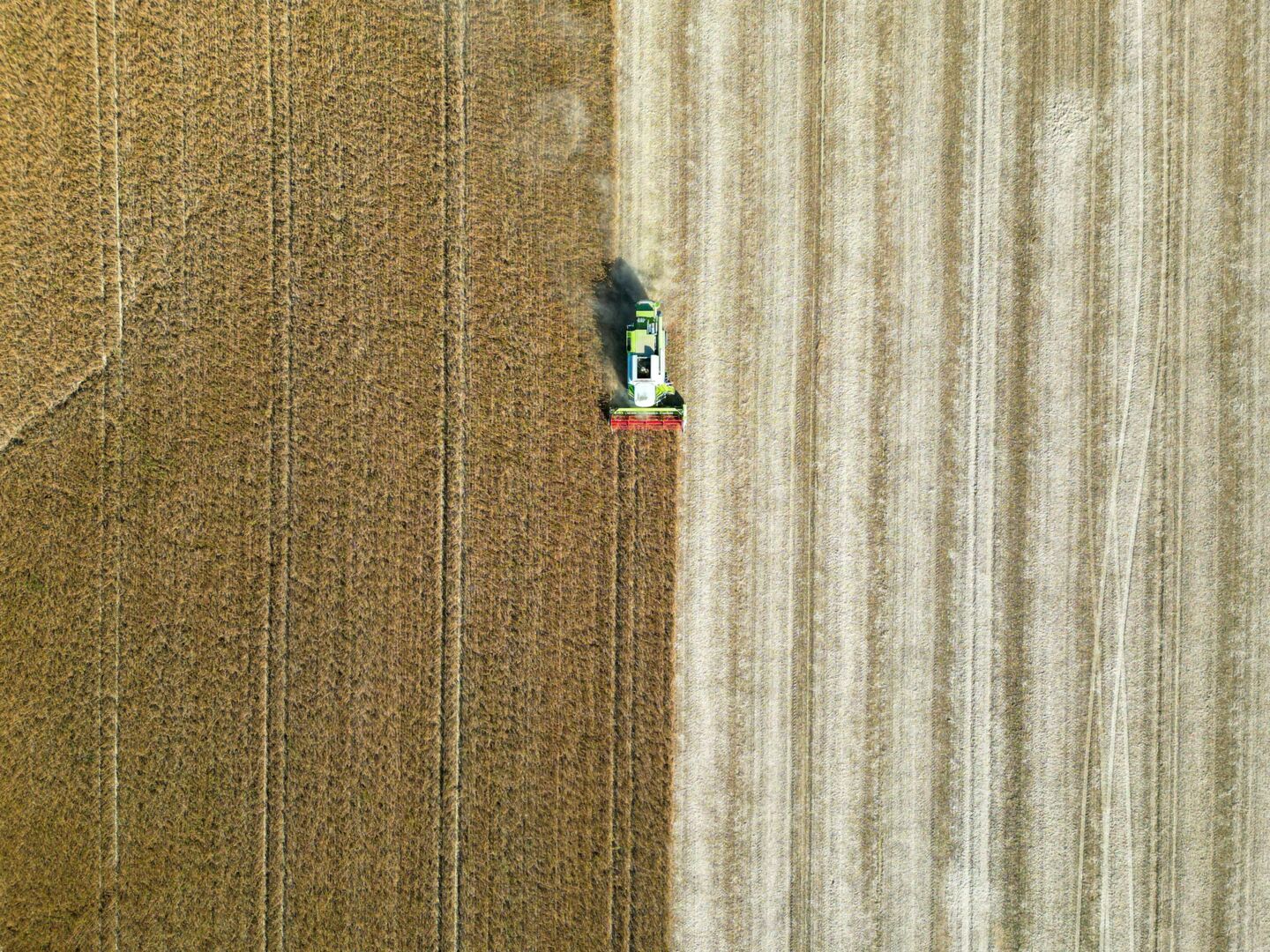 Drönarbild på en traktor som har skördat en halv åker.