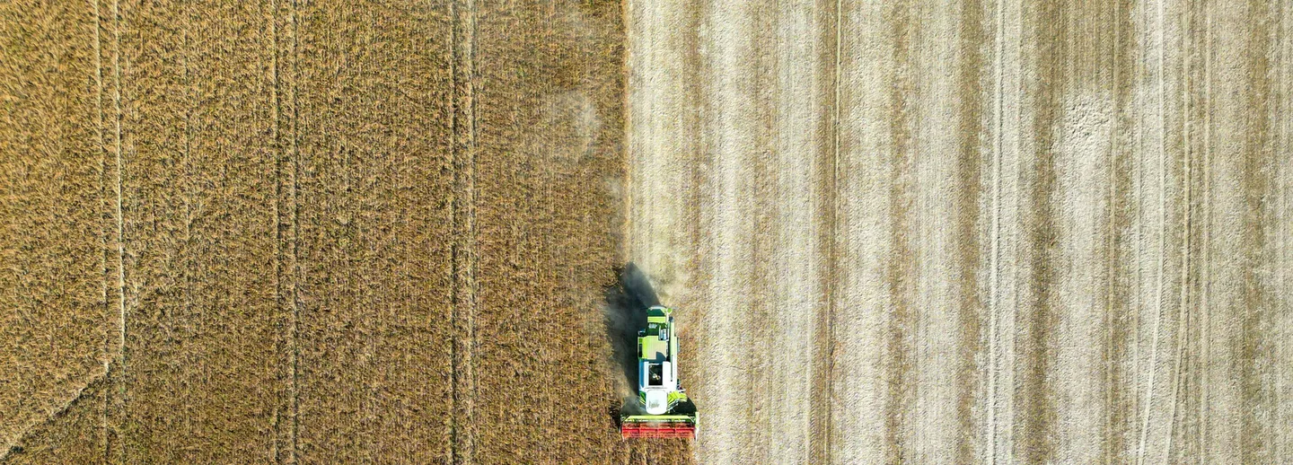 Drönarbild på en traktor som har skördat en halv åker.