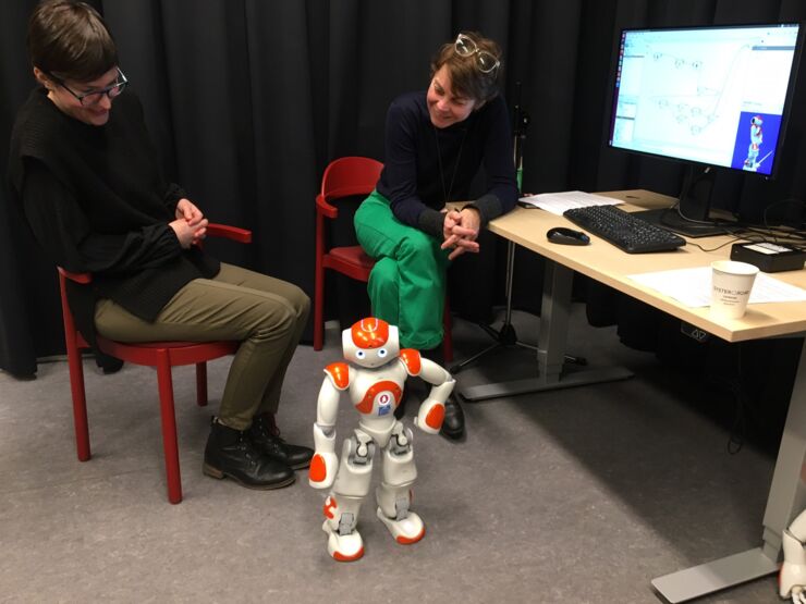Two researchers are looking at a orange robot