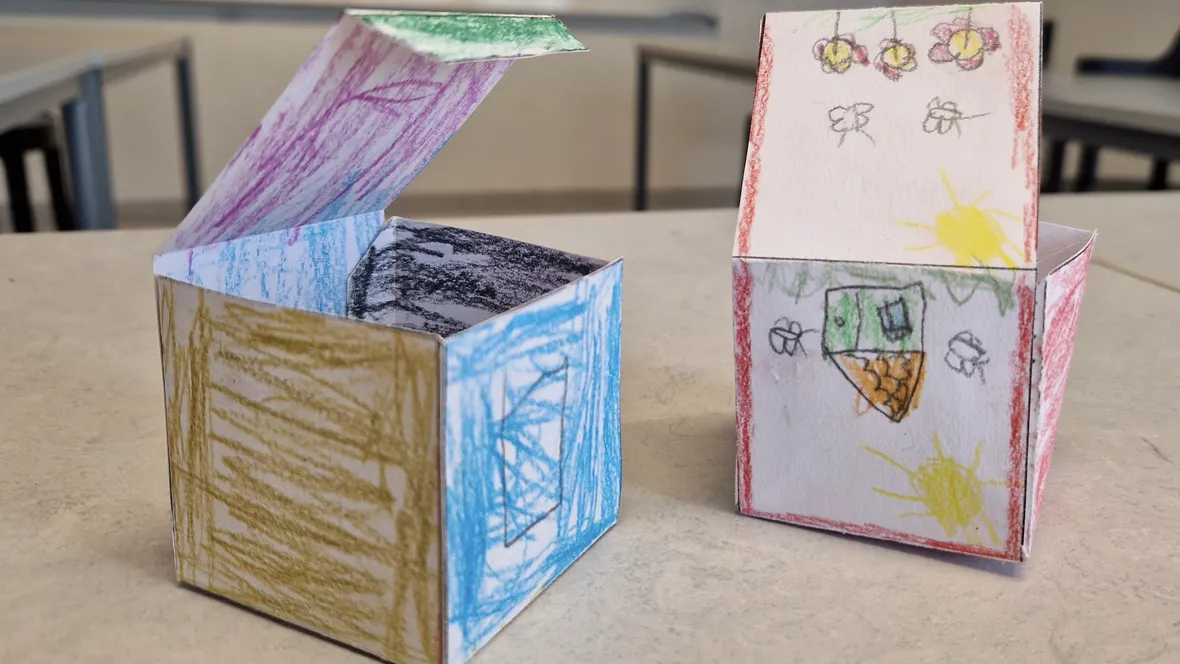 Två askar av papp med ritade blommor, hus och sol. 