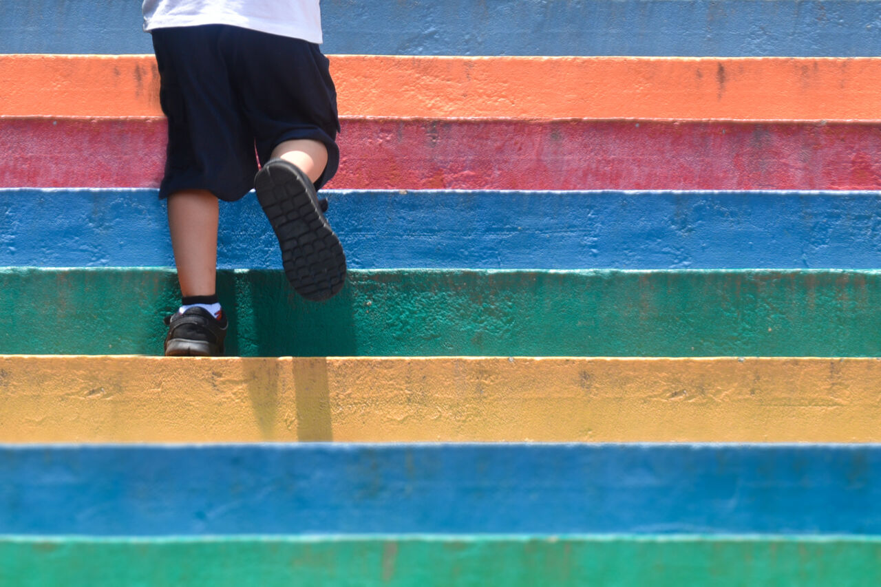 Lower part of a boy in walking shoes going up a colorful staircase outdoors.