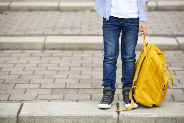 En pojke som håller i en gul ryggsäck. Ansiktet syns inte.