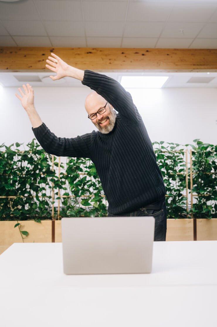 Person (Erik Berglund) stands infront of computer and reaches his arms in the air.