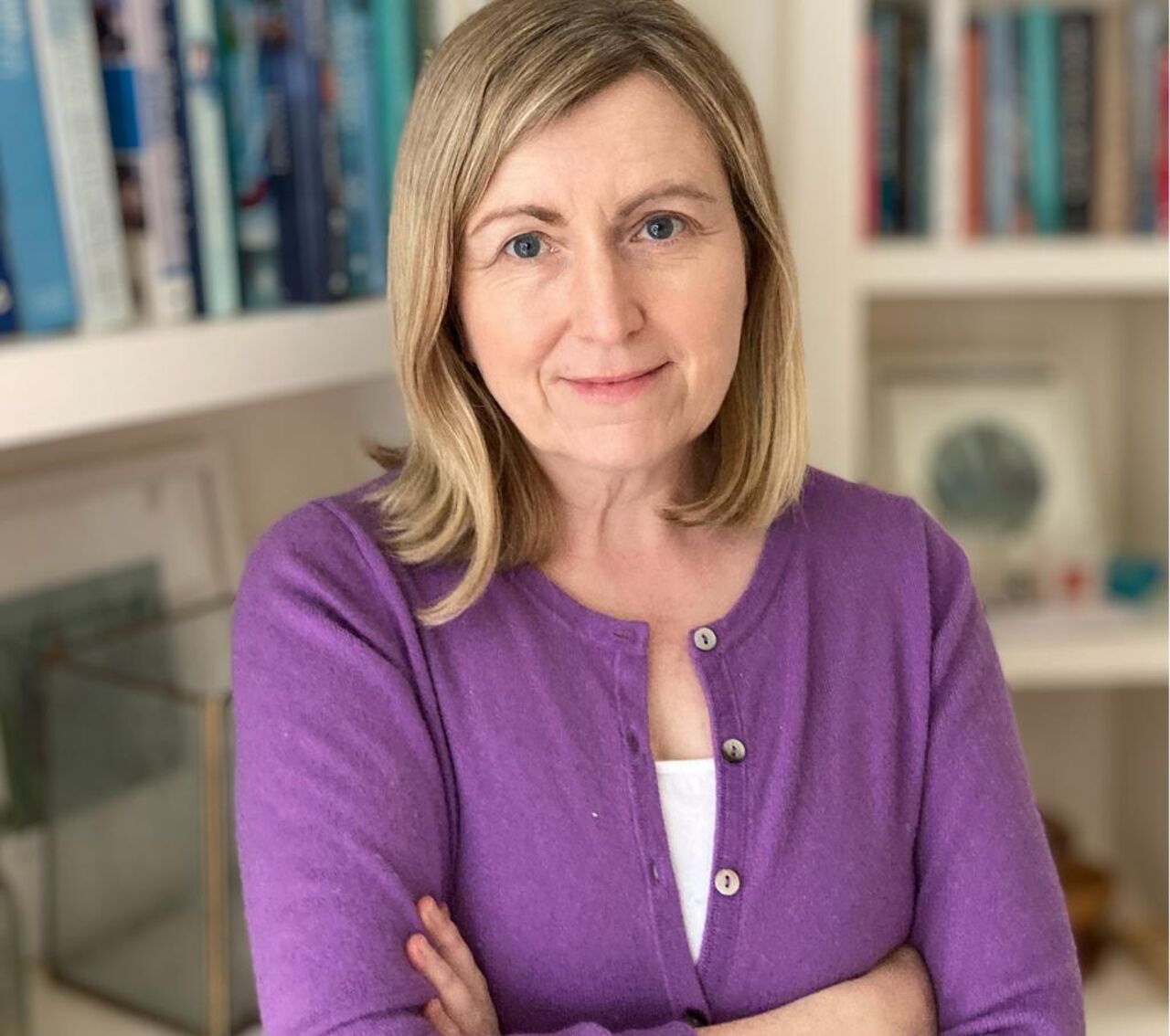 Professor Laura Lundy dressed in purple cardigan in front of two book shelves.