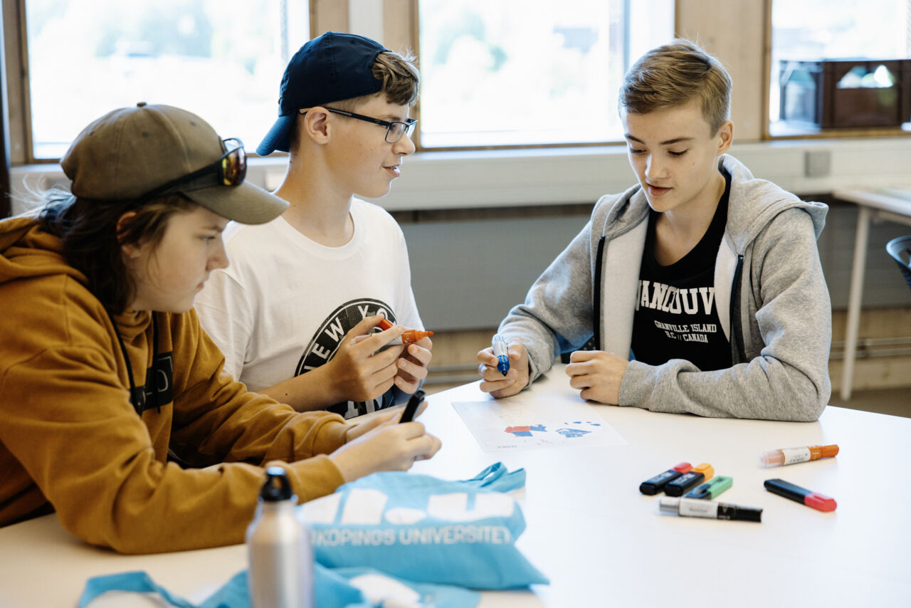 Bild på tre deltagare framför ett bord under en aktivitet