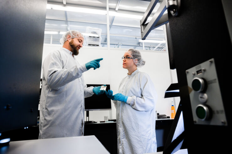 Male and female researcher wearing white lab coats are discussing in a lab.