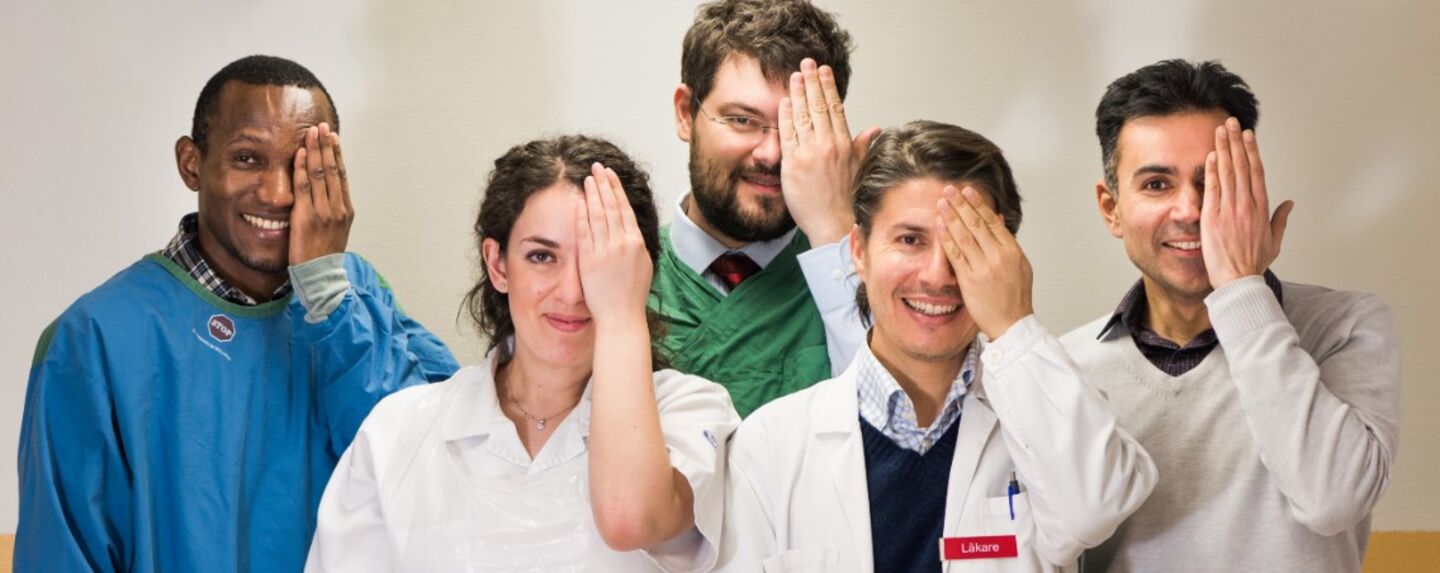 The research group stands and holds one hand in front of its own eye.