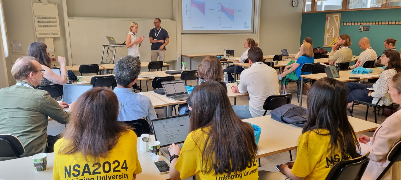 Two researchers presenting research in front of many visitors.
