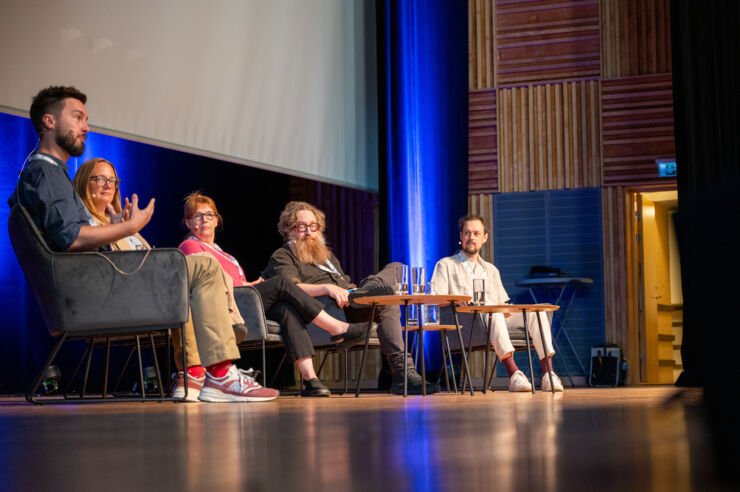 Five persons sitting on a stage and talking.