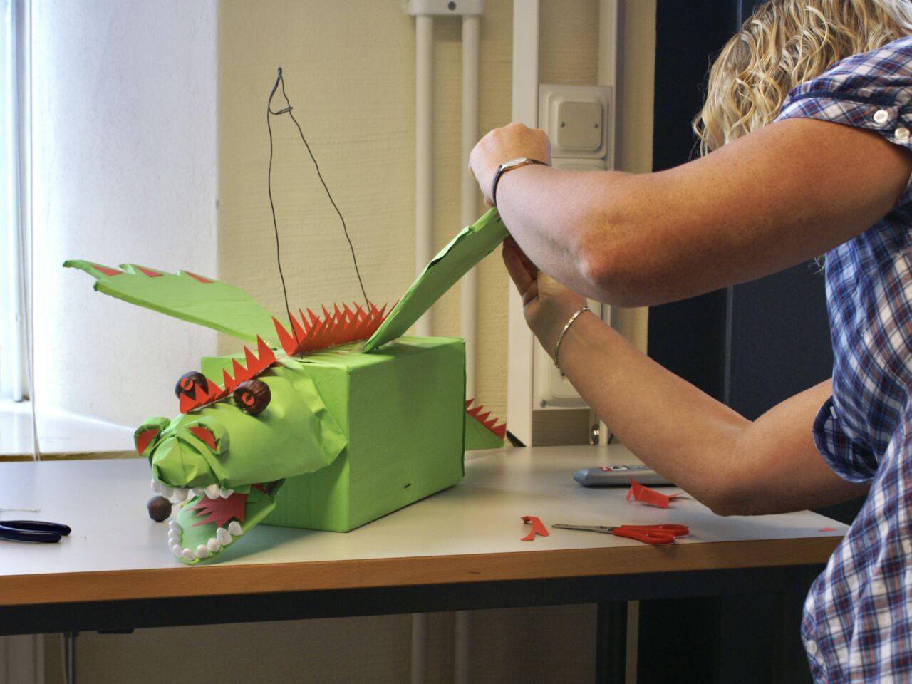 En person konstruerar en grön pappersdrake. 