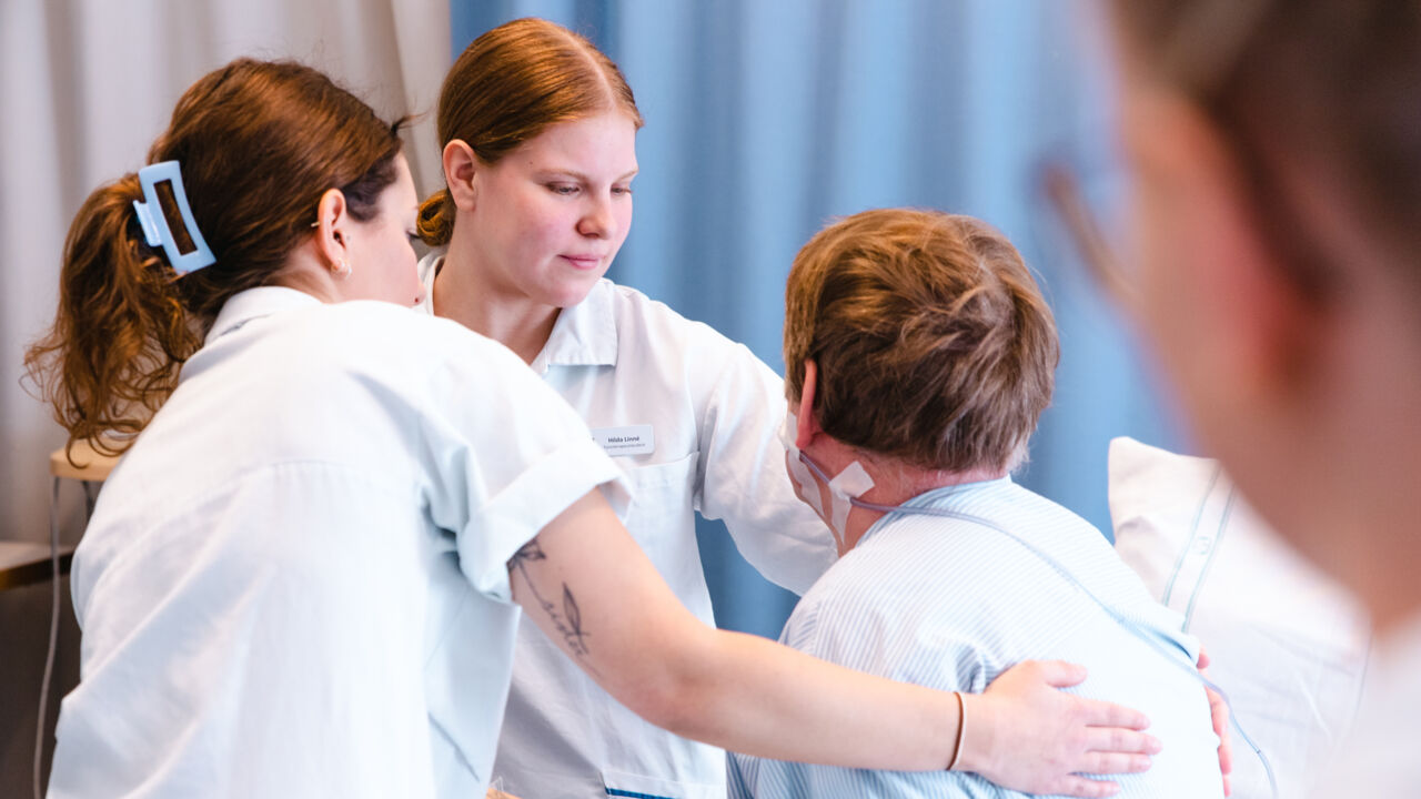 Fysioterapeutstudenter hjälper en patient att resa sig ur säng.