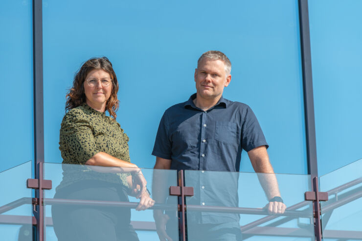 Sofia Nyström och Henrik Nordvall in front of a window that reflects the blue sky.