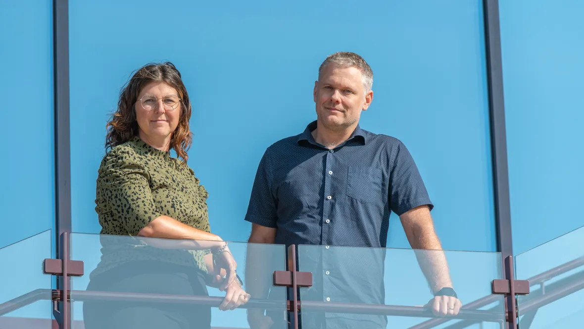 Sofia Nyström och Henrik Nordvall framför ett fönster som återspeglar en blå himmel.