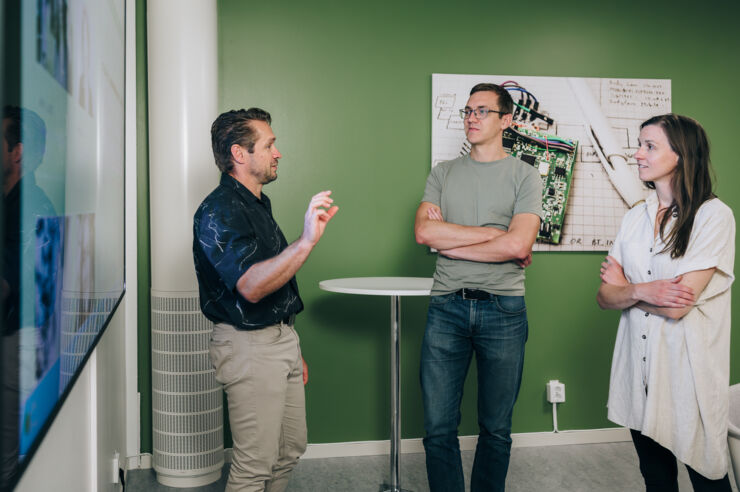 Two men and a woman talk in front of a screen