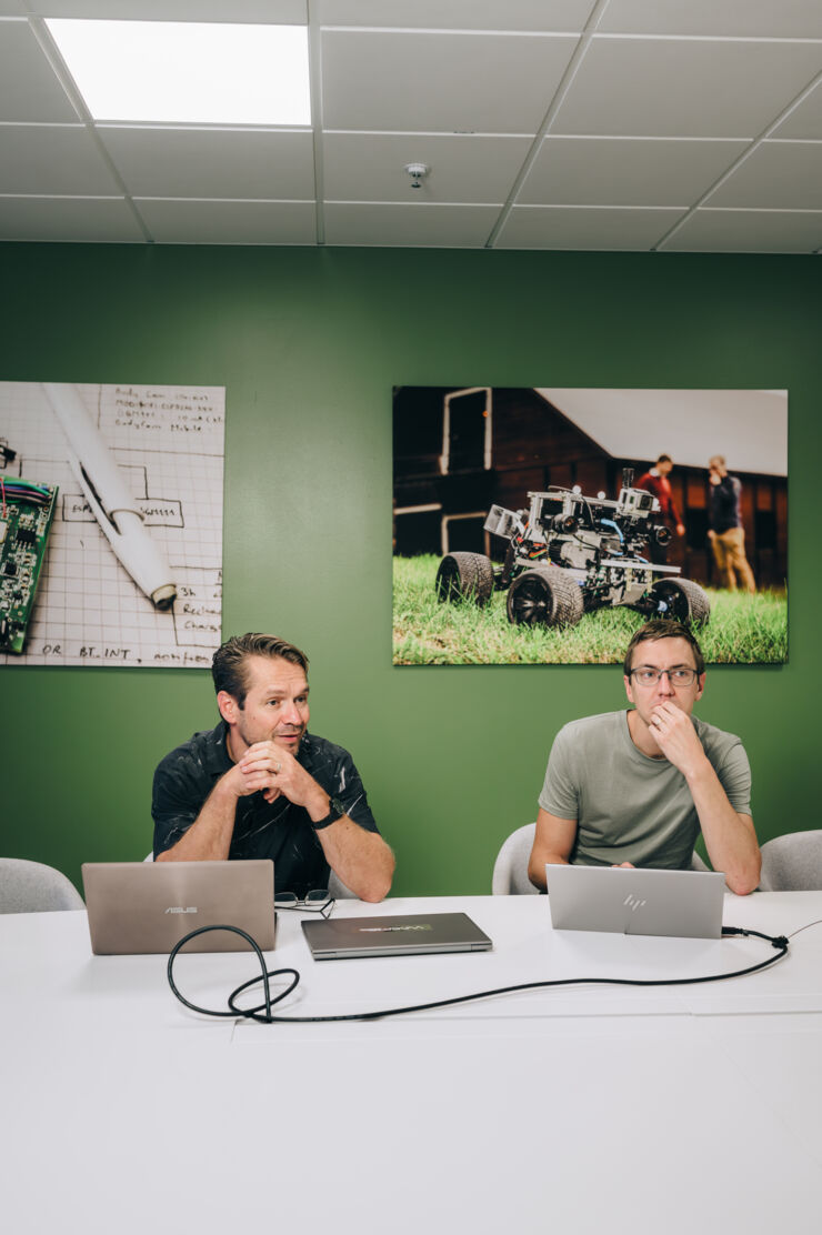 Two men sit at a table with laptops