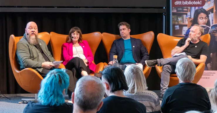 Four persons in chairs on a stage.