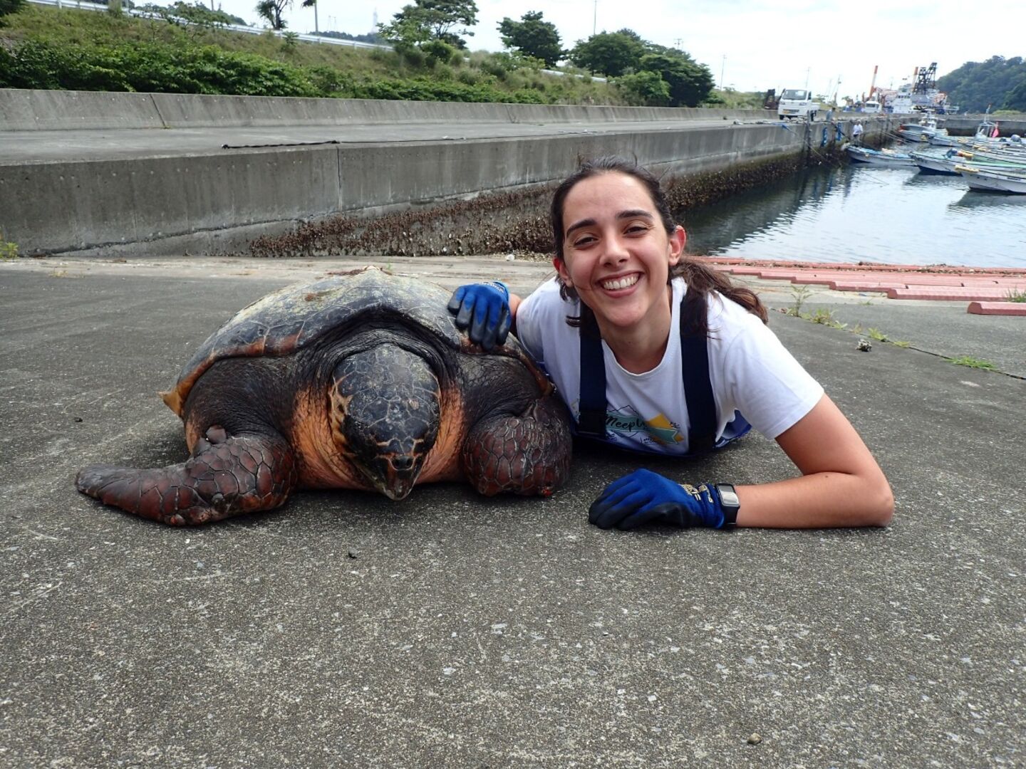 A woman with a big smile next to a loggerhead turtle.