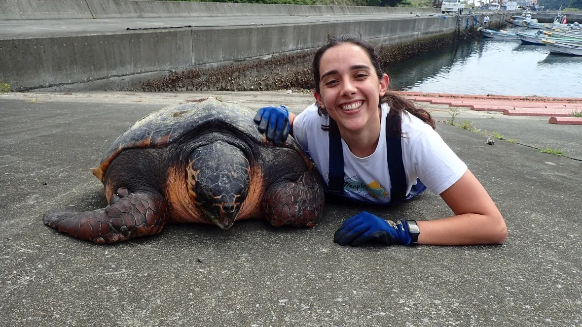 A woman with a big smile next to a loggerhead turtle.