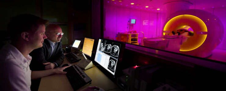 Photo of two persons in the control room in front of a MR camera