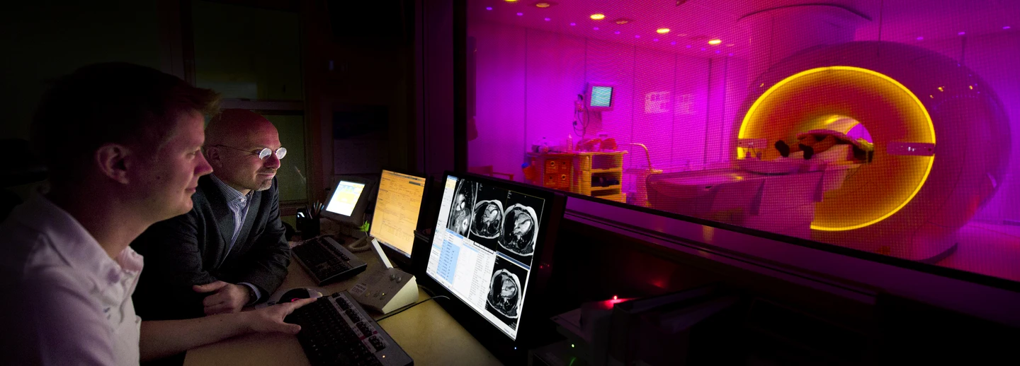 Photo of two persons in the control room in front of a MR camera